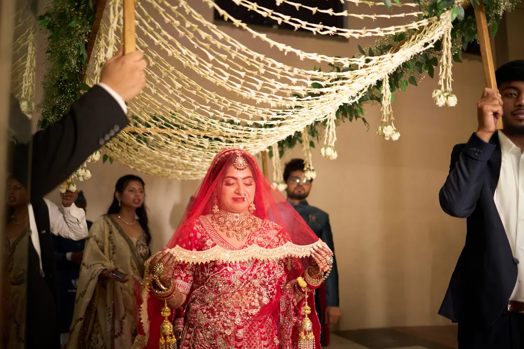 Bride walking in under a phoolon ki chadar held by her brothers, covered in a one side wedding photography package in Varanasi